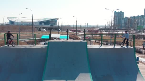 Letecký pohled na skatepark. Dva profesionální muži začínají jezdit na kolech z vrcholu rampy — Stock video
