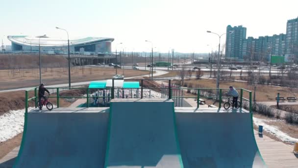 Vista aerea su uno skatepark. Due uomini professionisti iniziano ad andare in bicicletta da una cima delle rampe e a cavalcare in avanti — Video Stock