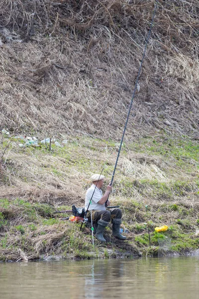 Un pescador sentado cerca del río sosteniendo una caña — Foto de Stock