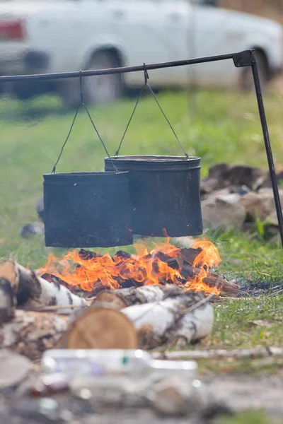 Die Menschen heizen Wasser in den Metalleimern mit einem Lagerfeuer auf. Eimer hängen an der Querstange — Stockfoto