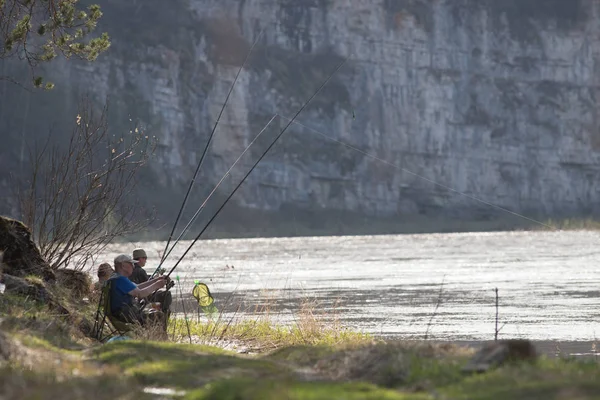 Fishermans sentado cerca del río sosteniendo una caña y esperando a que el pescado picotee — Foto de Stock