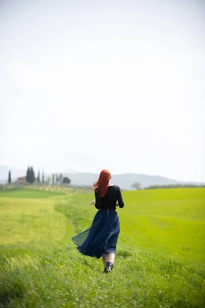 Una mujer en un vestido largo de pie en un prado verde brillante — Foto de Stock