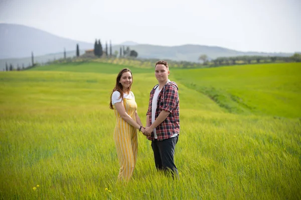 Mladý šťastný pár stojící na zelené louce, držící ruce — Stock fotografie