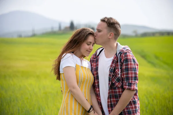 Un jeune couple heureux debout sur une prairie verte. Un homme embrasse sa copine dans un front — Photo