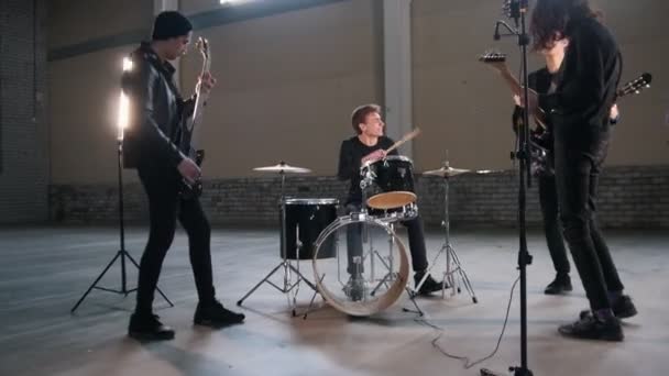 Молодая группа играет рок-музыку в большой комнате с яркими огнями — стоковое видео