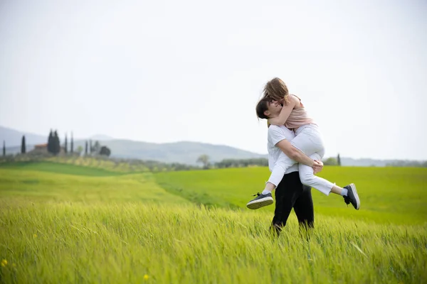 Un jeune couple souriant heureux sur une prairie verte. Un homme tenant sa petite amie sur les mains — Photo