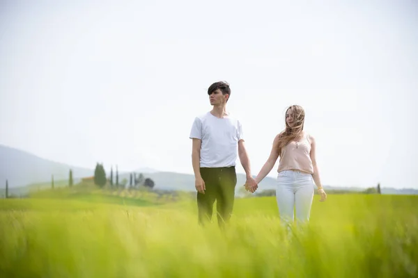 Молода пара стоїть на зеленому полі, тримаючись за руки — стокове фото