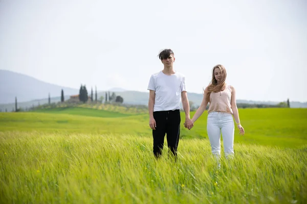 Молода пара стоїть на зеленому лузі, тримаючись за руки — стокове фото