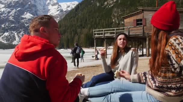 若い人が旅行してる海岸に座りパンを食べる — ストック動画