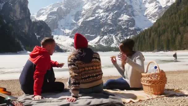 Молоді люди подорожують. Сидячи на узбережжі і їдячи бутерброди — стокове відео