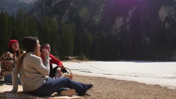 Jovens a viajar. Amigos fazendo um piquenique na costa e comendo sanduíches ao redor das montanhas — Vídeo de Stock