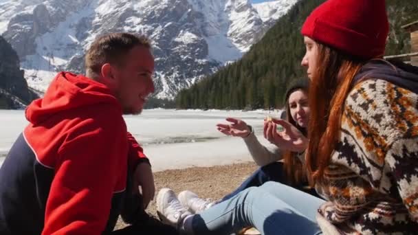 Amigos haciendo un picnic en la costa y comiendo sándwiches alrededor de las montañas — Vídeo de stock