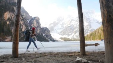 Bir lago di braies 'de yürüyen genç bir kadın. Büyük bir sırt çantasıyla donmuş sahilde ve etrafa bakıyor.