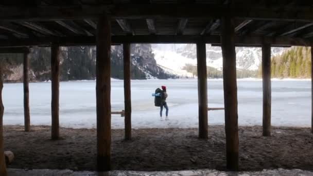 Ung kvinna står på en lago di braies frusen kust med en stor resande ryggsäck — Stockvideo