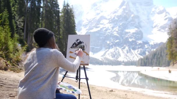 Dolomitas. Uma jovem mulher desenhando montanhas e floresta em uma tela em um cavalete — Vídeo de Stock