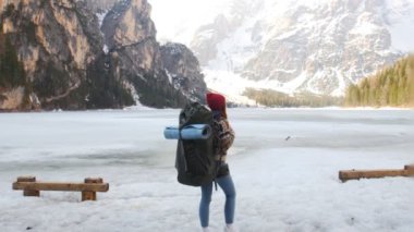 Bir lago di braies 'de duran genç bir kadın büyük bir sırt çantasıyla donmuş sahilde.