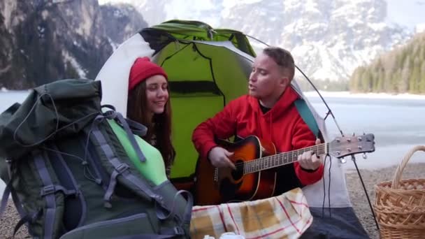 Giovane coppia seduta nella tenda e che canta alla chitarra su uno sfondo di montagne — Video Stock