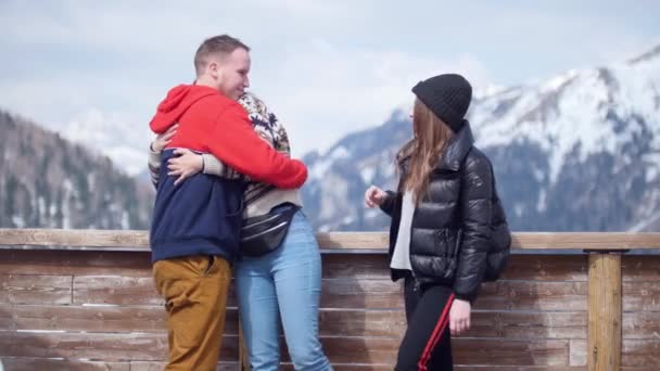 Dos mujeres jóvenes turísticas de pie sobre un fondo de montañas. Su amigo viene a ellos y se abrazan — Vídeo de stock