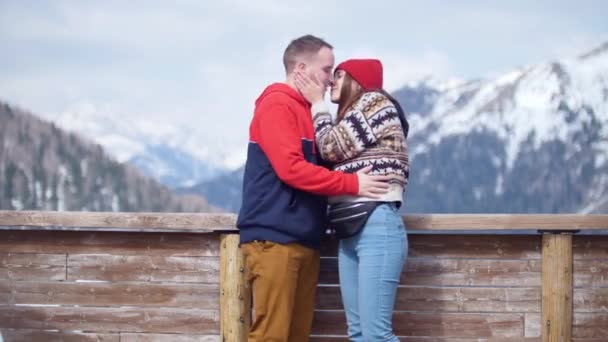 Um jovem casal de turistas em pé sobre um fundo de montanhas e beijo — Vídeo de Stock