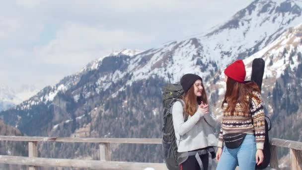 Duas jovens turista viajando em Dolomites com mochila grande e guitarra. De pé na estrada e a falar — Vídeo de Stock