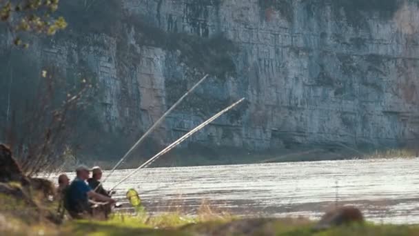 Fishermans sentado cerca del río sosteniendo una caña y esperando a que el pescado picotee — Vídeos de Stock