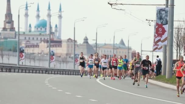 05-05-2019 РОССИЯ, КАЗАНЬ: Беговой марафон. Разные люди бегут по обочине дороги на фоне Казанского Кремля — стоковое видео