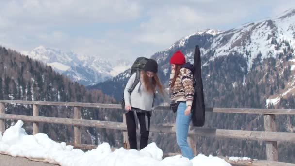Twee jonge vrouwen toerist reizen in de Dolomieten met grote rugzak en gitaar. Staande op de weg en dansen — Stockvideo