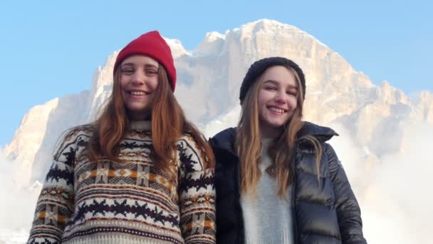 Dos jóvenes mujeres sonrientes de pie sobre un fondo de una montaña y posando — Vídeo de stock