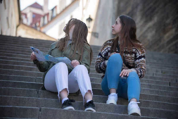 Dos jóvenes sentadas en las escaleras sosteniendo un mapa y mirando hacia atrás —  Fotos de Stock