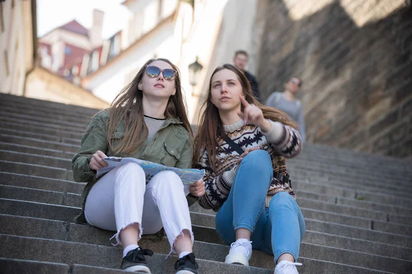 Dos mujeres jóvenes sentadas en las escaleras sosteniendo un mapa y mirando directamente —  Fotos de Stock