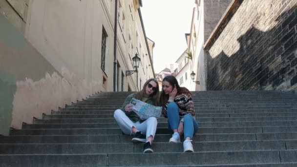 Zwei junge Frauen, die auf der Treppe sitzen und auf die Karte schauen — Stockvideo