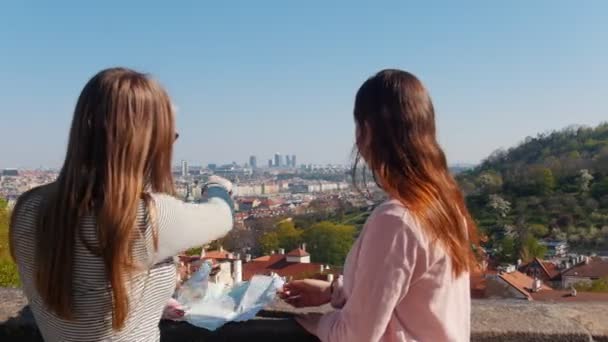 Deux jeunes femmes debout sur le pont d'observation ouvert et regardant la carte. Pointant vers les endroits de la ville — Video