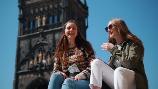 Two women sitting on a background of Bridge Tower of Charles Bridge. Talking and laughing — Stock Video