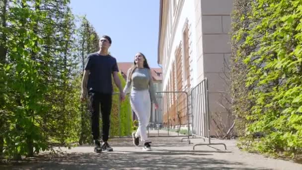 Una joven pareja caminando entre árboles decorativos cogidos de la mano — Vídeos de Stock