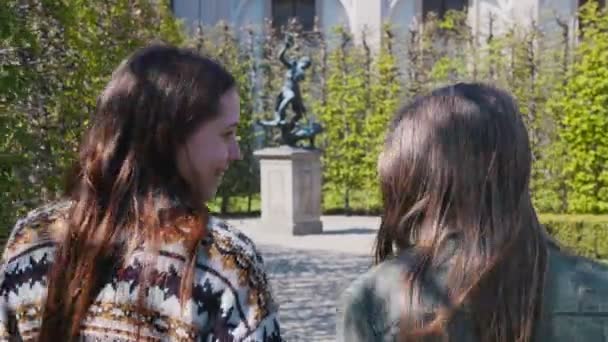 Dos mujeres jóvenes caminando en el parque entre plantas decorativas y tomando fotos de estatuas — Vídeo de stock