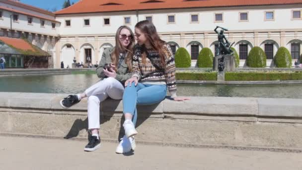 Zwei junge Frauen sitzen in der Nähe des Brunnens und schauen auf das Telefon — Stockvideo