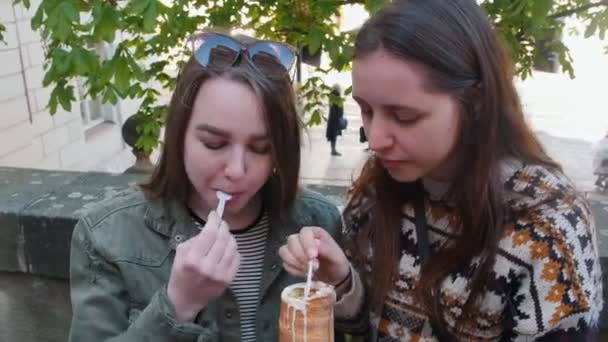 Dos mujeres jóvenes sentadas en el parque y comiendo helado checo con una cucharita de plástico — Vídeos de Stock