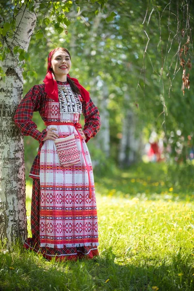 Young woman in traditional russian clothes standing in the forest and holds hands on a waist — стокове фото