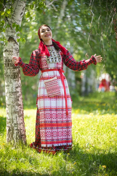 Молодая женщина в традиционной русской одежде стоит в лесу и поднимает руки — стоковое фото