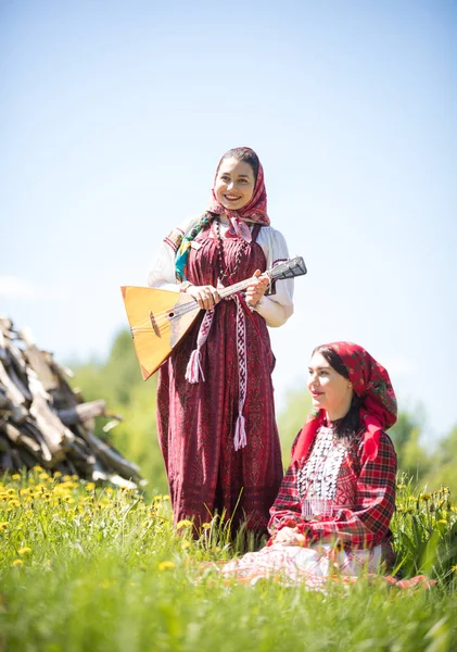 В поле две молодые женщины в традиционной русской одежде, одна из них сидит — стоковое фото