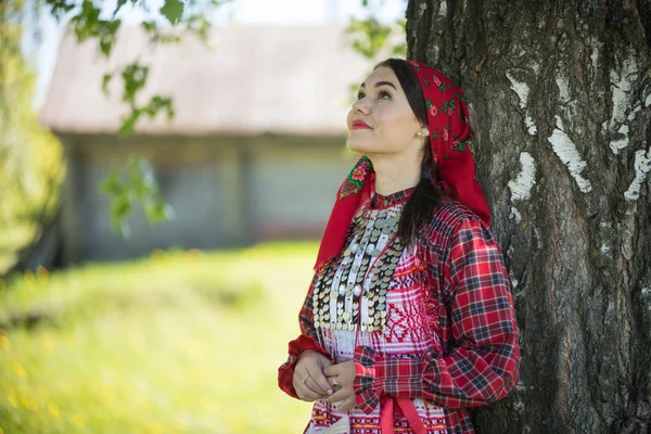 Geleneksel Rus kıyafetleri içinde bir ağacın altında dikilip yukarı bakan genç bir kadın. — Stok fotoğraf