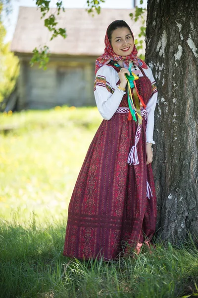 Geleneksel Rus elbiseli genç bir kadın bir ağacın altında duruyor ve at kuyruğunu tutuyor. — Stok fotoğraf