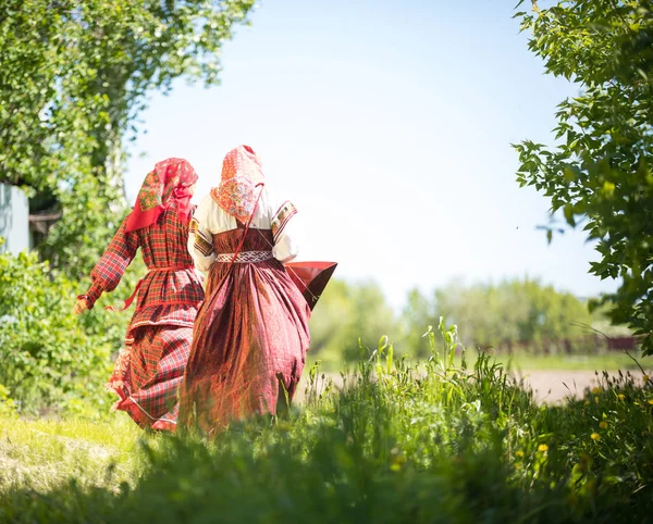 Two young women in traditional russian clothes stand in the field between the trees — Stock Photo, Image