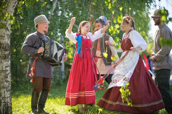 Ludzie w tradycyjnych rosyjskich ubrań tańczą w lesie-jeden z nich odgrywa akordeon i śpiew — Zdjęcie stockowe
