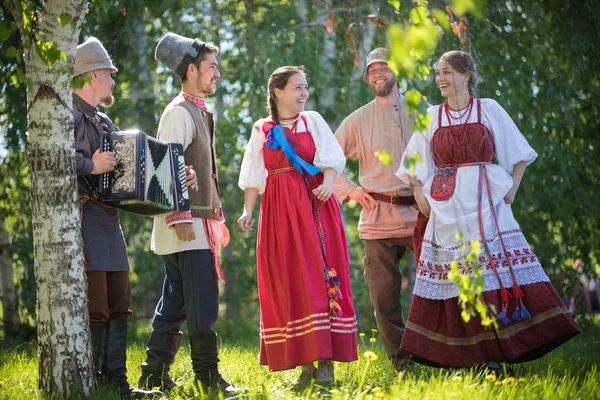 Люди в традиционной русской одежде танцуют в поле и разговаривают - один из них играет аккордеонную музыку — стоковое фото