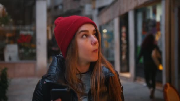 Uma jovem mulher comendo sobremesa doce enquanto caminha na rua e segurando um telefone — Vídeo de Stock