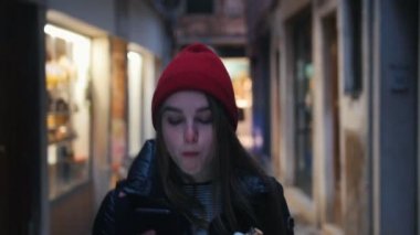 Sokakta yürürken ve telefon tutarken kırmızı şapkalı genç bir kadın tatlı tatlı yiyor