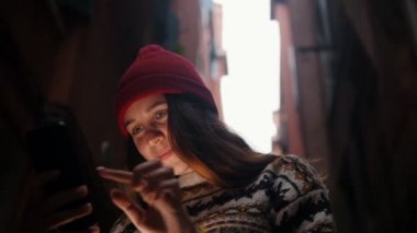 Sokakta duran ve telefon ekranına bakan genç bir kadın. Bir ışık yüzünü aydınlatır