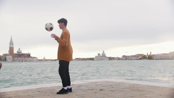 Un hombre jugando con una pelota de fútbol en el estrado sobre un fondo del mar. Patear la pelota con las piernas y la cabeza — Vídeo de stock