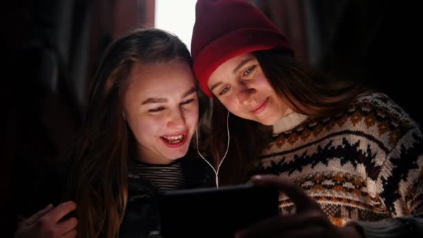 Zwei junge lächelnde Frauen, die auf der Straße stehen und mit Kopfhörern auf den Telefonbildschirm schauen — Stockvideo